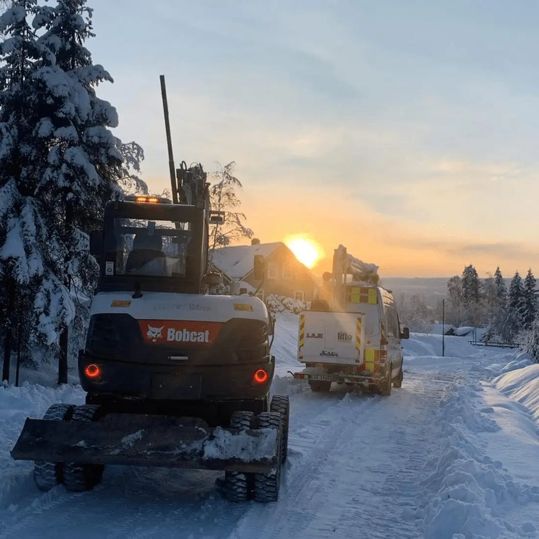 Hjullaster og lastebil på snødekt vei i soloppgang
